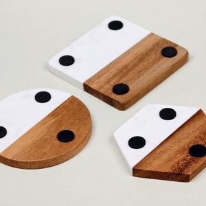 May include: Three round, square, and hexagonal coasters made of wood and white marble with black rubber feet on the bottom.