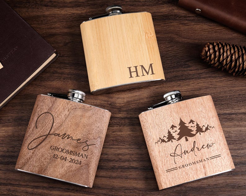 May include: Three wooden engraved flasks with metal caps. The flasks are personalized with the names "James", "Andrew", and the initials "HM".
