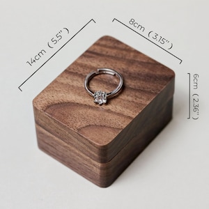 May include: A wooden ring box made of walnut wood with a ring inside. The box measures 5.5 inches long, 3.15 inches wide, and 2.36 inches high.