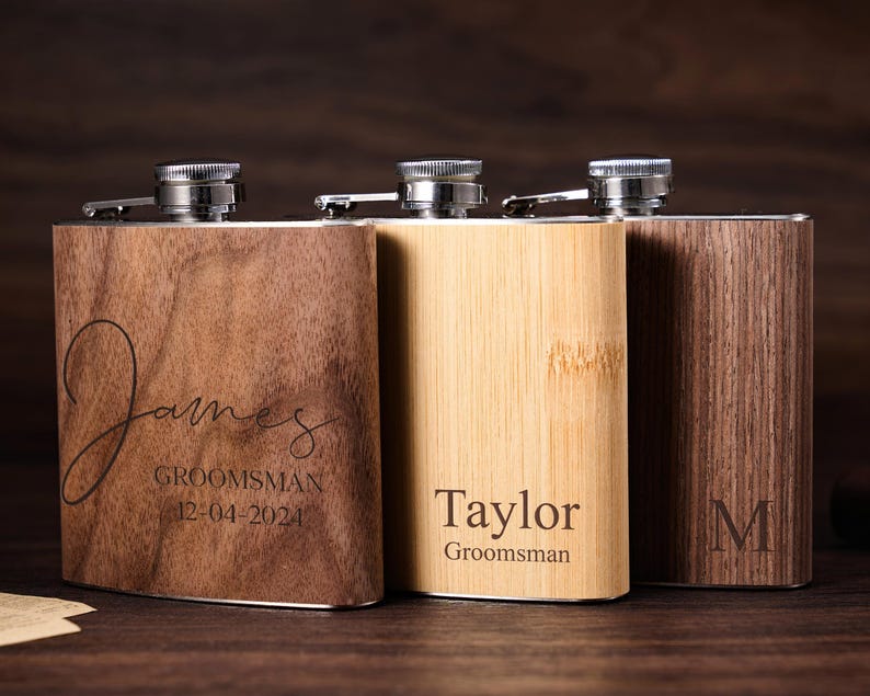May include: Three personalized wooden flask sets with engraved names and titles. The flasks are made of walnut, bamboo, and oak wood. The names engraved on the flasks are "James", "Taylor", and "M".