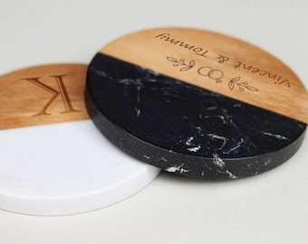 May include: Two round wooden coasters with a black and white marble design. One coaster has the letter "K" engraved on the wood and the other has the text "Vincent & Tonya" with a small drawing of two rings and leaves.