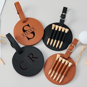 May include: Four personalized leather golf ball bag tags. Two tags are brown with black lettering, one says "STEVEN" and the other says "CR". The other two tags are black with white lettering and feature a design of six golf tees.