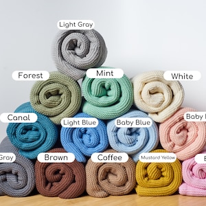 May include: A collection of 12 rolled up knitted blankets in various colors, including light gray, forest green, mint green, white, canal blue, baby pink, light blue, baby blue, dark gray, brown, coffee brown, mustard yellow, and ballet pink.