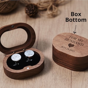 May include: A wooden box with a hinged lid, open to reveal two cufflinks. The box is engraved with "FOR MY HUSBAND" and a heart, with the date "JULY 28, 2025". The cufflinks have a white background with black text. The box is oval-shaped.