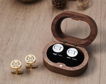 May include: Gold-toned cufflinks with a personalized design, displayed with a wooden oval box. The cufflinks feature the initial "M" and the name "Matthew" within a laurel wreath. The box contains cufflinks with the initials "CT".
