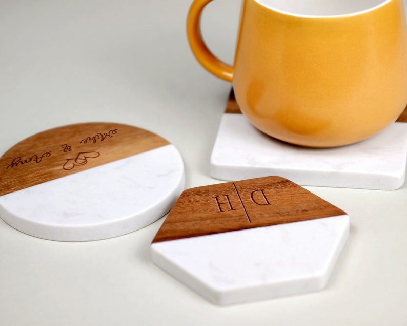 May include: Two round coasters with a wood and marble design. One coaster has the text "Our love is our own" engraved on the wood portion. The other coaster has the initials "D/H" engraved on the wood portion.
