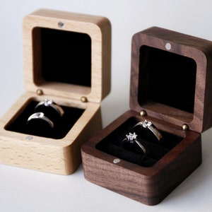 Op de afbeelding: Twee houten ringendoosjes, een van licht hout en een van donker hout, beide met een fluwelen binnenkant en twee ringen.