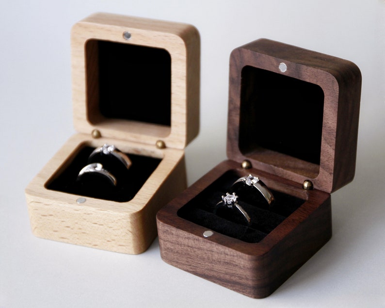 Op de afbeelding: Twee houten ringendoosjes, een van licht hout en een van donker hout, beide met een fluwelen binnenkant en twee ringen.