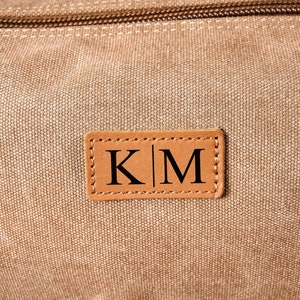 Puede incluir: Una bolsa de lona marr&oacute;n con un parche de cuero que dice "K|M" en letras negras.