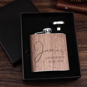 May include: A wooden flask with a stainless steel lid and funnel. The flask is engraved with the name "James" and the text "Groomsman 12-04-2024".