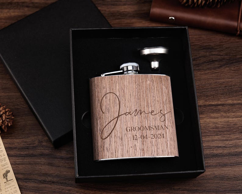 May include: A wooden flask with a stainless steel lid and funnel. The flask is engraved with the name "James" and the text "Groomsman 12-04-2024".