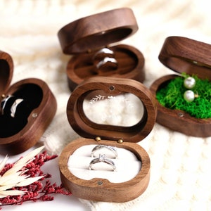 May include: Three wooden ring boxes with different interiors. One box has a black velvet interior, another has a white velvet interior, and the third has a green moss interior. The box with the white velvet interior has a clear glass lid with the words "Mr. & Mrs." engraved on it.