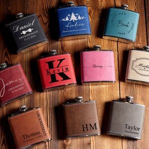 May include: Ten personalised leather-bound hip flasks with various names and dates engraved on them. The flasks are arranged on a wooden surface.