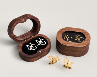 May include: Oval wooden cufflink boxes with gold and silver initial cufflinks. One box is open, showing silver initials on a black velvet interior. The other box is closed, with gold initials visible through a clear top. Two pairs of gold cufflinks are displayed.