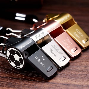 May include: Four silver whistles with black, gold, and rose gold finishes. Each whistle has a different inscription, including "Best coach", "COACH Adam", "COACH Thomas", and "Mr. Williams".