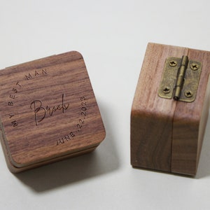 May include: Two wooden ring boxes. One box has the text "My Best Man Brook June 22, 2023" engraved on the top. The other box has a brass hinge.