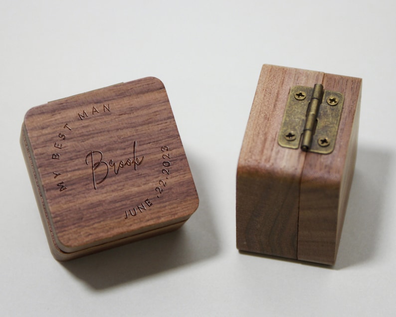 May include: Two wooden ring boxes. One box has the text "My Best Man Brook June 22, 2023" engraved on the top. The other box has a brass hinge.