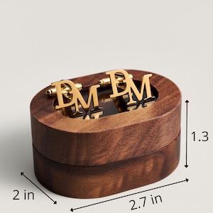 May include: A wooden oval box with gold-colored cufflinks. The cufflinks feature the letters "DM". The box is 2.7 inches long, 2 inches wide, and 1.3 inches tall. The box and cufflinks are on a light background.