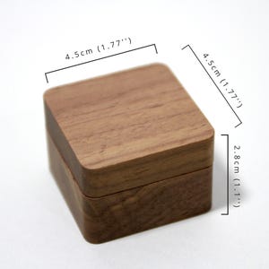 May include: A small wooden box with a hinged lid. The box is 4.5 inches wide and 2.8 inches tall.