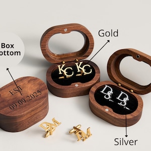 May include: Wooden oval-shaped boxes with clear lids, each containing initial cufflinks. One set is gold, another silver. The box bottoms are engraved with initials and a date. The cufflinks are in the shape of letters.