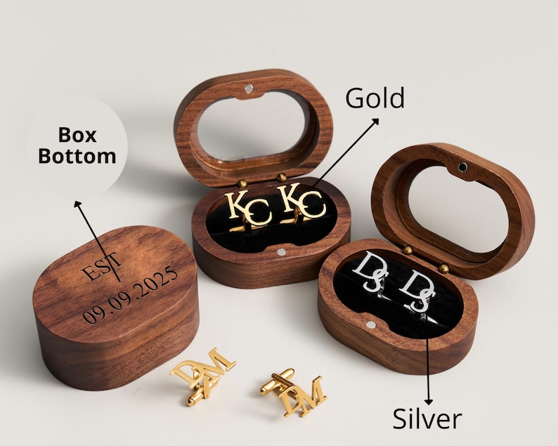 May include: Wooden oval-shaped boxes with clear lids, each containing initial cufflinks. One set is gold, another silver. The box bottoms are engraved with initials and a date. The cufflinks are in the shape of letters.