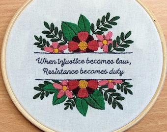 May include: Embroidered hoop art with a floral design and the quote "When injustice becomes law, resistance becomes duty".