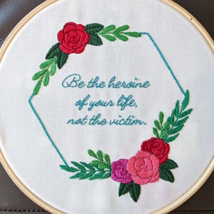 Puede incluir: Arte de bordado en aro con un diseño floral y la cita "Sé la heroína de tu vida, no la víctima."