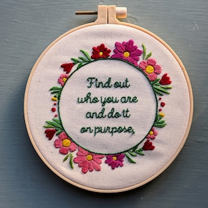 Puede incluir: Arte de bordado en aro con una corona de flores y la cita "Descubre quién eres y hazlo a propósito."