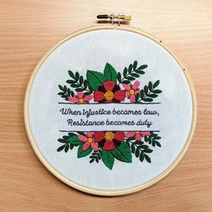 May include: Embroidered hoop art with a floral design and the quote "When injustice becomes law, resistance becomes duty".