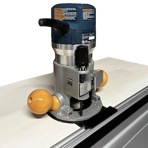 May include: A blue and silver Bosch router with a black handle and a depth adjustment knob. The router is mounted on a grey and black router table with a black guide rail. The router is set up to cut a piece of wood.