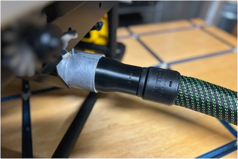 May include: A black and green Festool dust extraction hose with a black connector. The hose is connected to a gray and black dust extraction port.