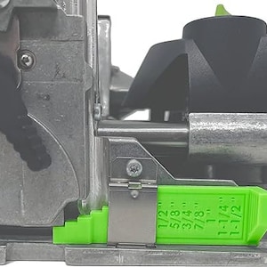 May include: A close-up of a green and silver router jig with a depth gauge marked in fractions of an inch. The gauge is labeled with the following measurements: 1/2", 5/8", 3/4", 7/8", 1", 1-1/4", and 1-1/2".