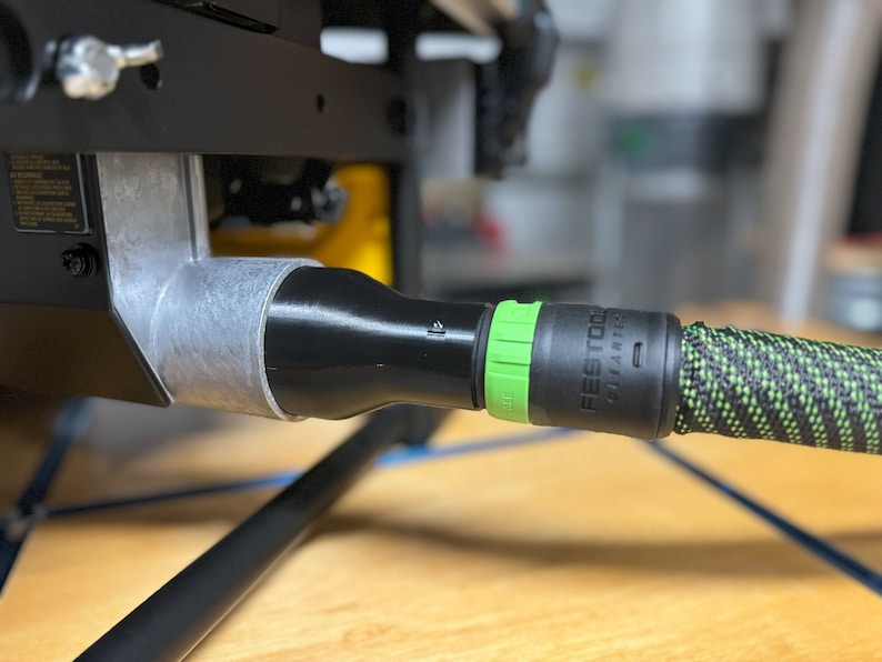 Puede incluir: Una manguera de aspiraci&oacute;n de polvo negra y verde con un conector verde conectado a un puerto de polvo negro. La manguera est&aacute; etiquetada como "Festool" y "Systainer".
