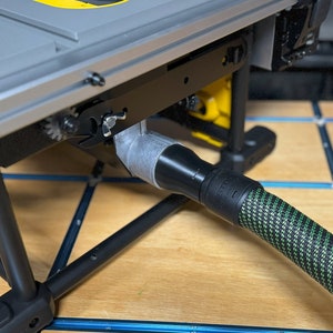 May include: A close-up of a black and green dust collection hose connected to a table saw. The hose is connected to a gray dust port on the table saw.