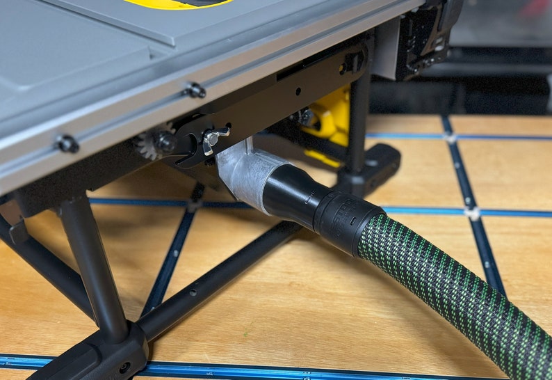 May include: A close-up of a black and green dust collection hose connected to a table saw. The hose is connected to a gray dust port on the table saw.