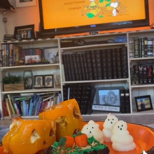May include: A plate of Halloween-themed treats, including orange bell pepper jack-o'-lanterns, a chocolate brownie with green frosting and candy pumpkins, and white marshmallow ghosts. The plate is on a blue surface with a book and a TV screen in the background. The TV screen shows the title card for the animated special "It's the Great Pumpkin, Charlie Brown."