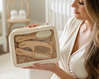 May include: A clear rectangular case containing a baby grooming kit. The kit includes a brush, comb, and other grooming tools. The tools are made of light-colored wood. The case is held by a person in a white dress.