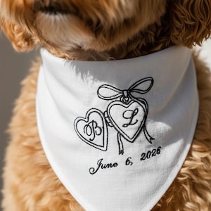 May include: White dog bandana with black embroidered hearts, initials, and the date June 6, 2026. The bandana is tied around a dog's neck, with the dog's fur visible.