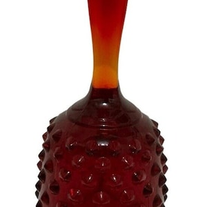 Peut inclure: Une cloche en verre rouge avec une surface texturée et un sommet pointu. La cloche a une poignée et une base large.