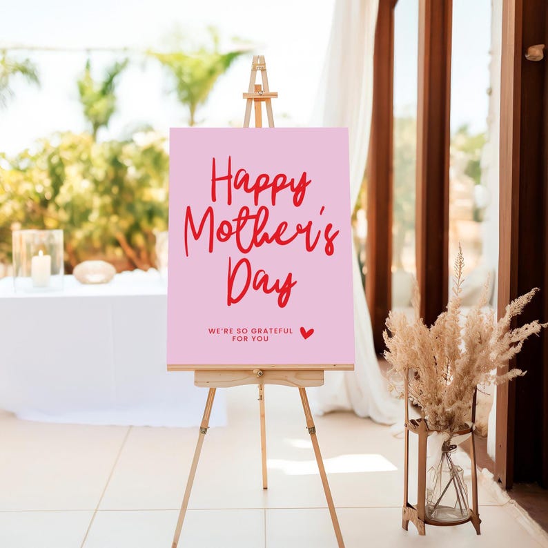 May include: A pink sign with the text "Happy Mother's Day" in red lettering. The sign also includes the text "We're so grateful for you" in smaller red lettering and a small red heart.