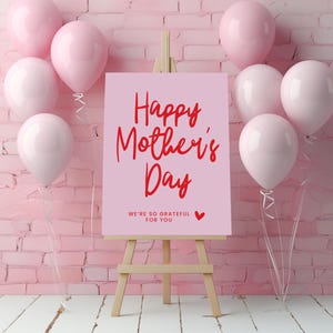 May include: Pink and white balloons surround a pink easel with a sign that reads "Happy Mother's Day" in red lettering. The sign also includes the text "We're so grateful for you" in smaller red lettering.