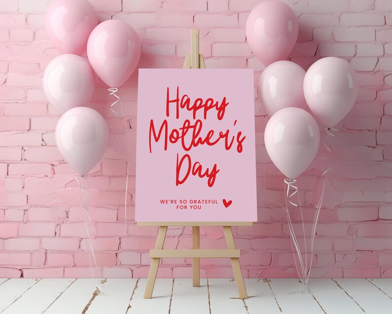 May include: Pink and white balloons surround a pink easel with a sign that reads "Happy Mother's Day" in red lettering. The sign also includes the text "We're so grateful for you" in smaller red lettering.
