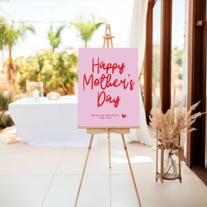 May include: A pink sign with the text "Happy Mother's Day" in red script font. The sign also includes the text "We're so grateful for you" in smaller red font with a small red heart.