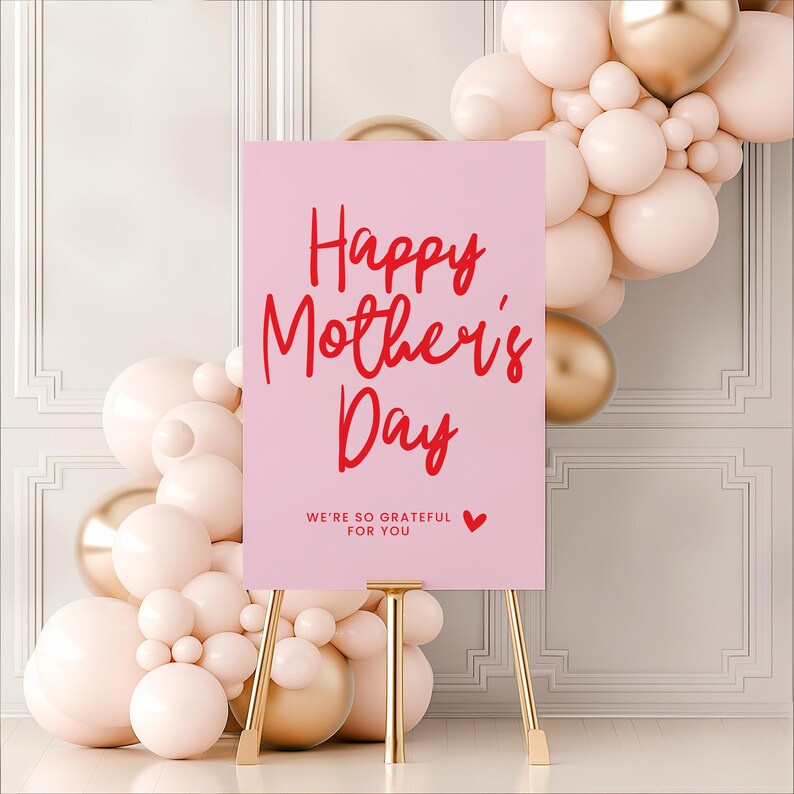 May include: Pink sign with the text "Happy Mother's Day" in red cursive lettering. The sign is on a gold easel and surrounded by pink and gold balloons.