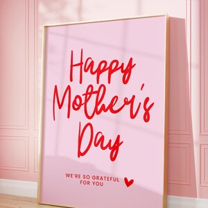 May include: A pink framed poster with the text "Happy Mother's Day" in red cursive lettering. The poster also includes the text "We're so grateful for you" in red lettering with a small red heart.
