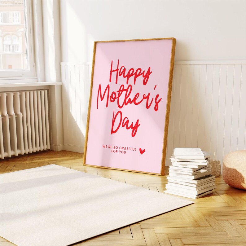 May include: A pink poster with a wooden frame, featuring the text "Happy Mother's Day" in red cursive lettering. The poster also includes the text "We're so grateful for you" in smaller red lettering and a small red heart.