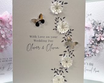 May include: A white card with a silver butterfly and floral design. The card says "With Love on your Wedding Day Oliver & Olivia".