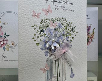 May include: A greeting card with the text "WITH LOVE TO A Very Special Mum ON YOUR 50TH BIRTHDAY". The card features a watercolor illustration of a floral arrangement in a glass jar, with butterflies and a ribbon.
