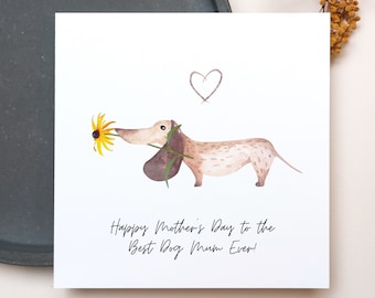 Könnte beinhalten: Weiße Grußkarte mit einer Aquarellillustration eines Dackels, der eine gelbe Blume hält. Die Karte hat ein handgezeichnetes Herz und den Text "Happy Mother's Day to the Best Dog Mum Ever!"