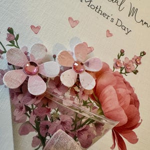 以下が含まれることがあります： 母の日のカード。ピンクと白の花束、大きな牡丹を含む。カードには「Love To A Special Mum On Mother's Day」の文字と小さなピンクのハートのアクセント。下部にはピンクのリボン。
